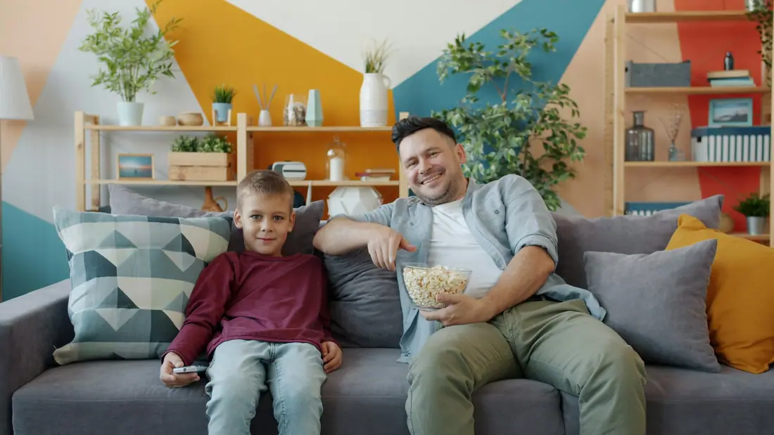 Father and son relaxing on a sofa with popcorn while watching television