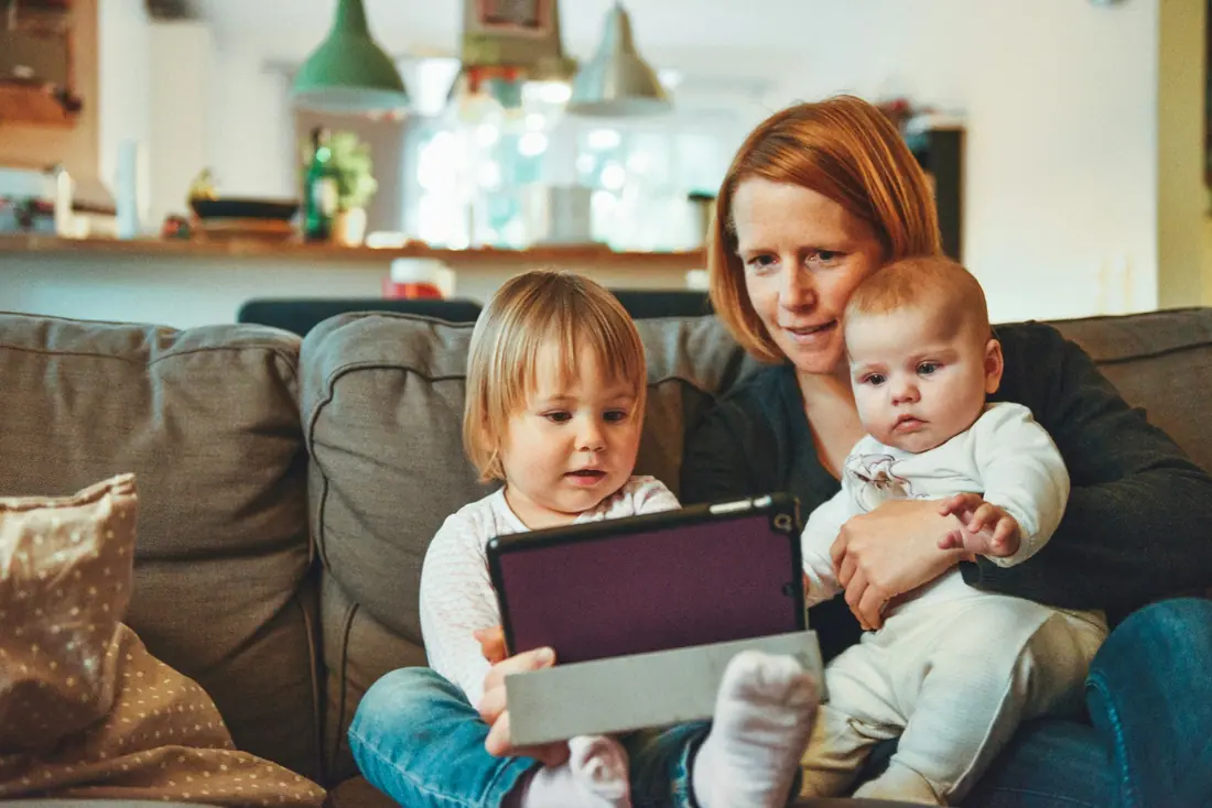 Mother and two young children looking at a tablet together on a sofa