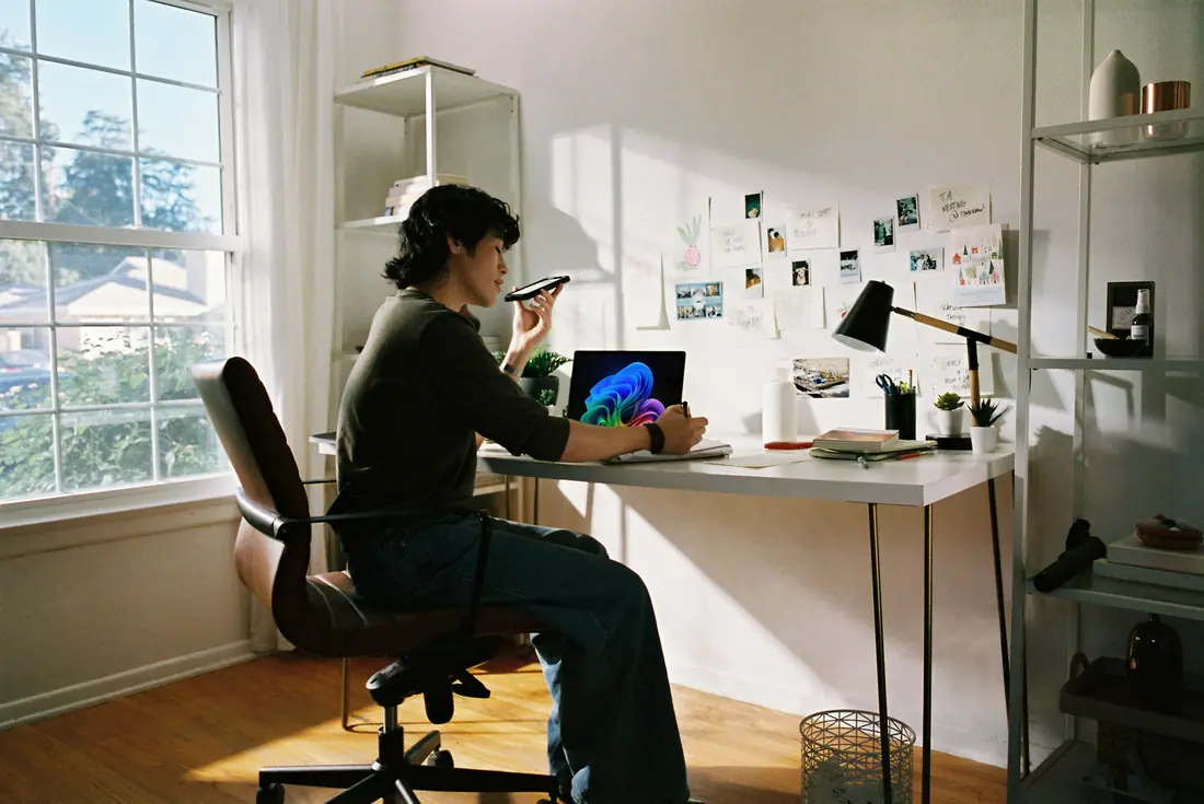 Person working at a laptop in a sunlit home office with a mood board on the wall