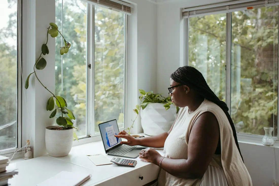 Woman working on a laptop beside large windows in a bright home office